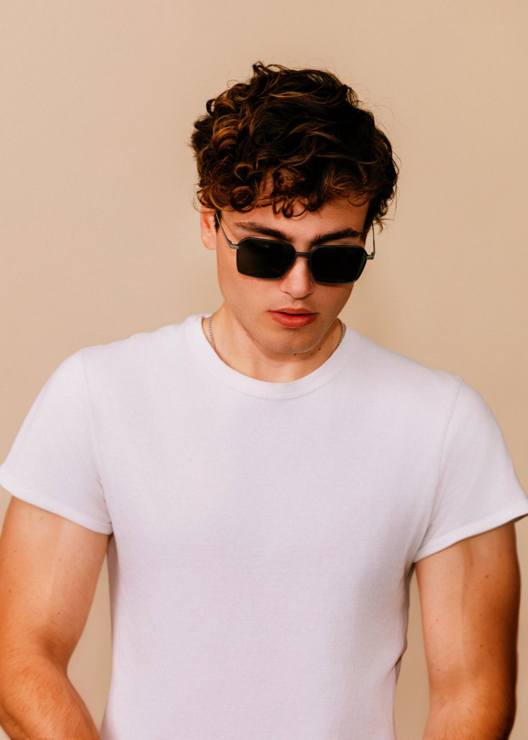 Male model wearing Rigel sunglasses in Olive Smoke with a white t-shirt, head tilted down. 