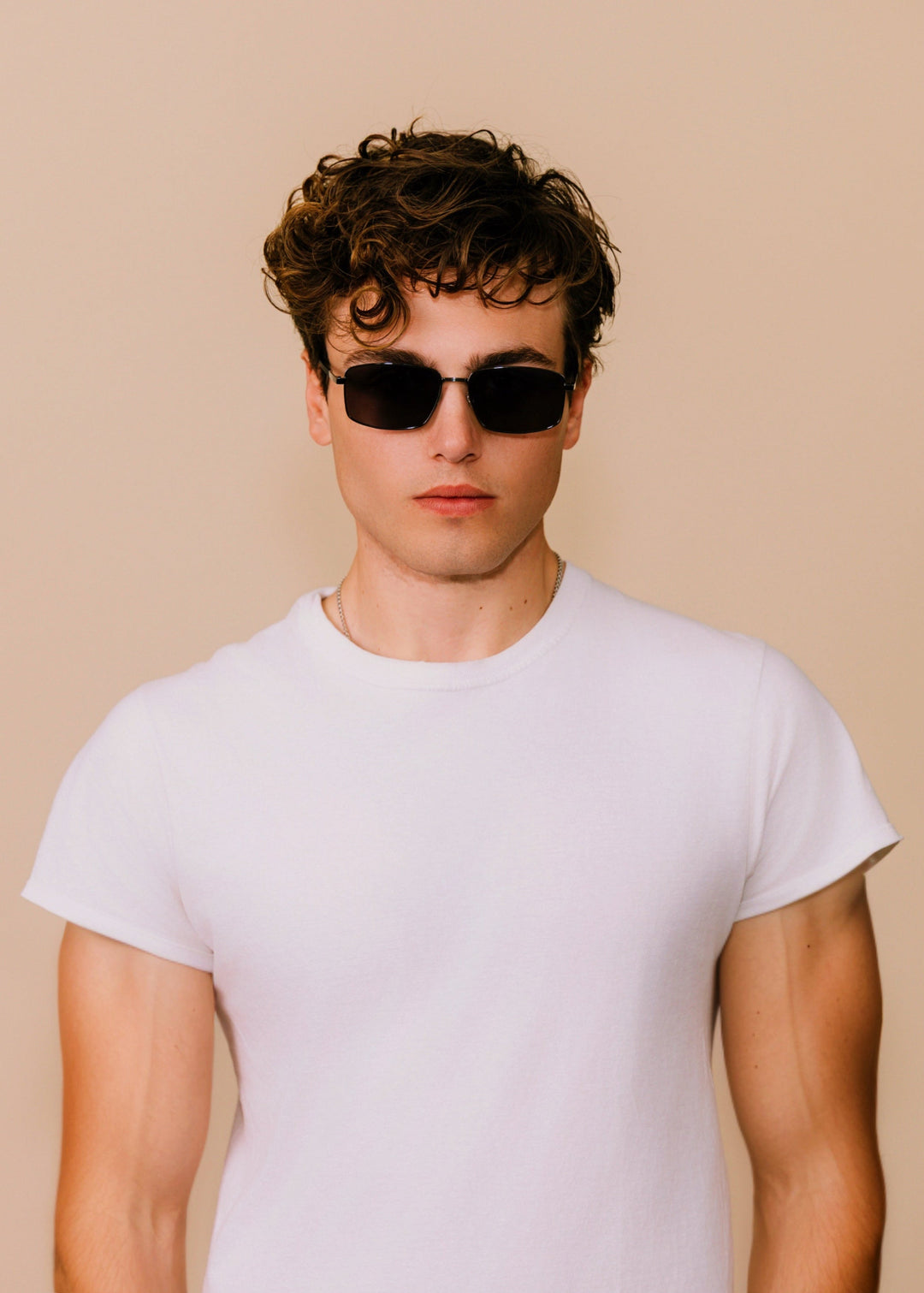 Male model wearing Sirius A sunglasses in Gunmetal Gray with a white T-shirt against a neutral background. 