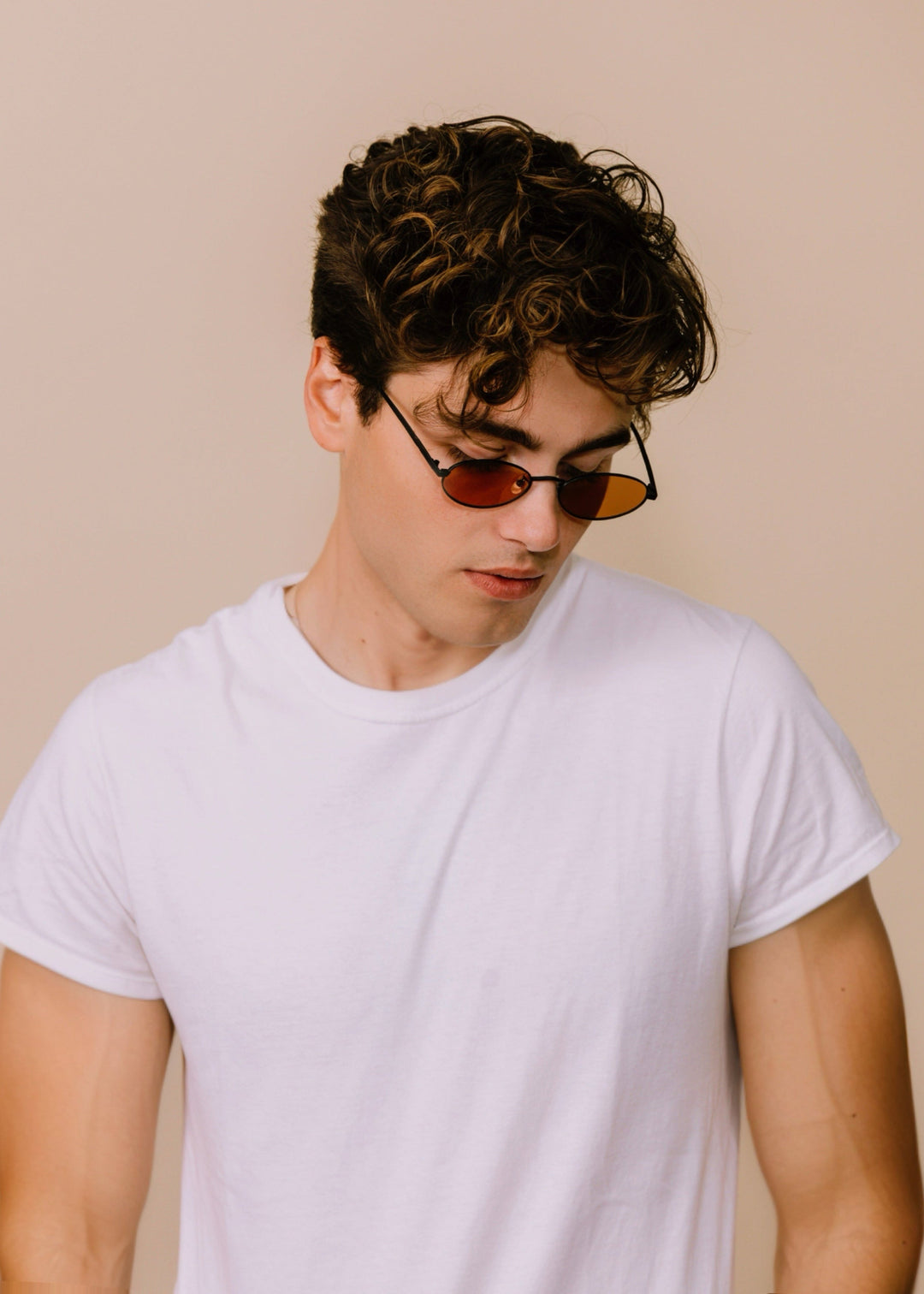 Three-quarter portrait of a model wearing Solstice sunglasses in Mahogany Black with a white T-shirt against a neutral background. 