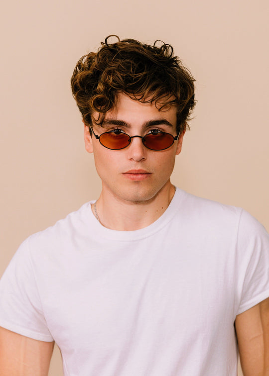 Front portrait of a model wearing Solstice sunglasses in Mahogany Black with a white T-shirt against a neutral background. 