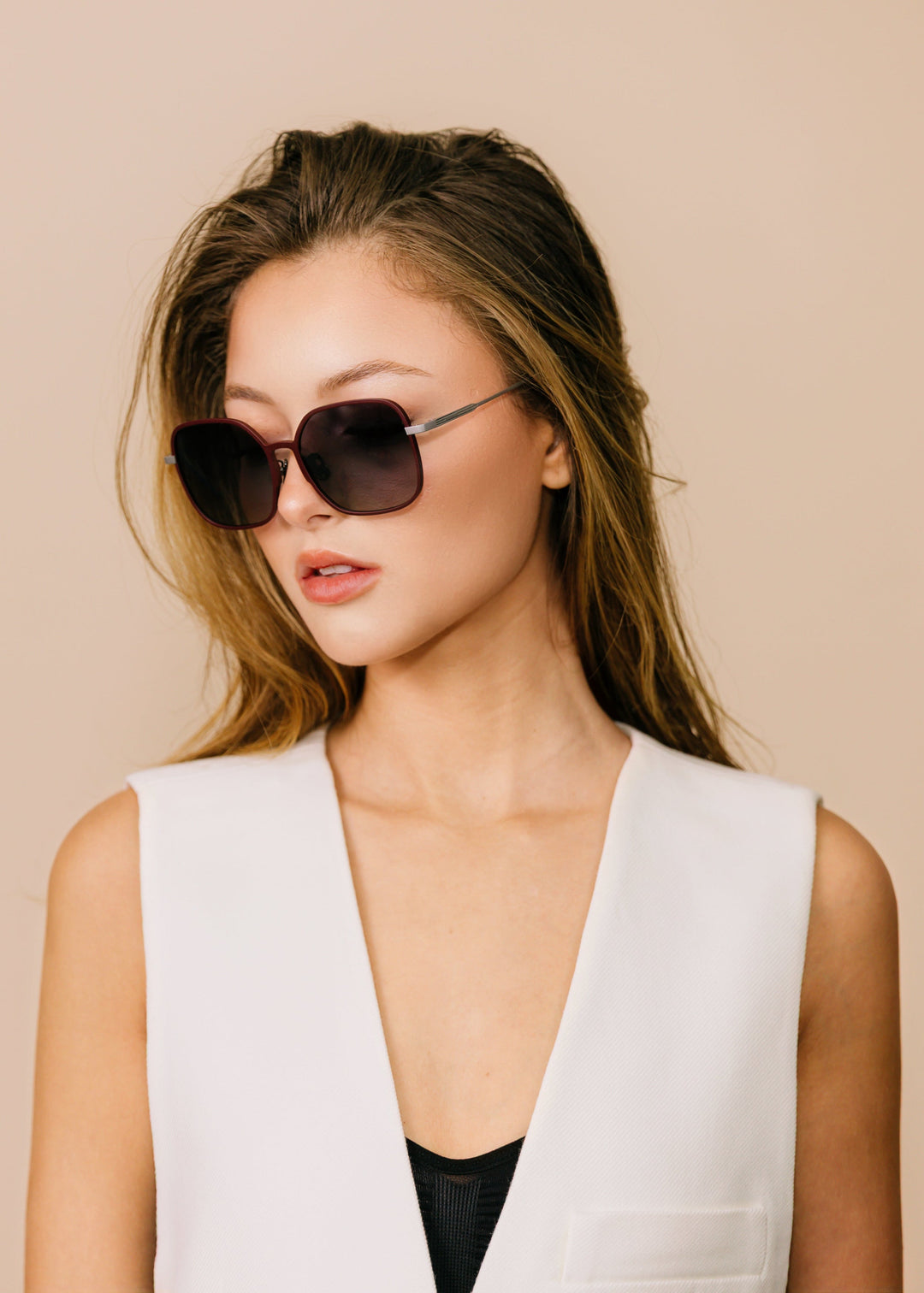 Female model wearing Spica sunglasses in Cherry Red with a white open vest over a black top, turned to the side. 