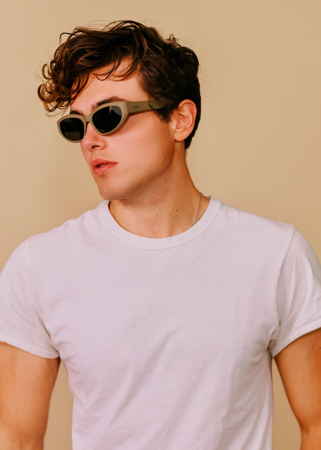 Man wearing Void Striker sunglasses in Bronze Mirage with a white T-shirt against a warm beige background. 