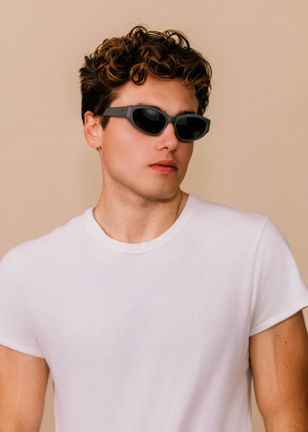 Man wearing sunglasses and a white t-shirt against a beige background 