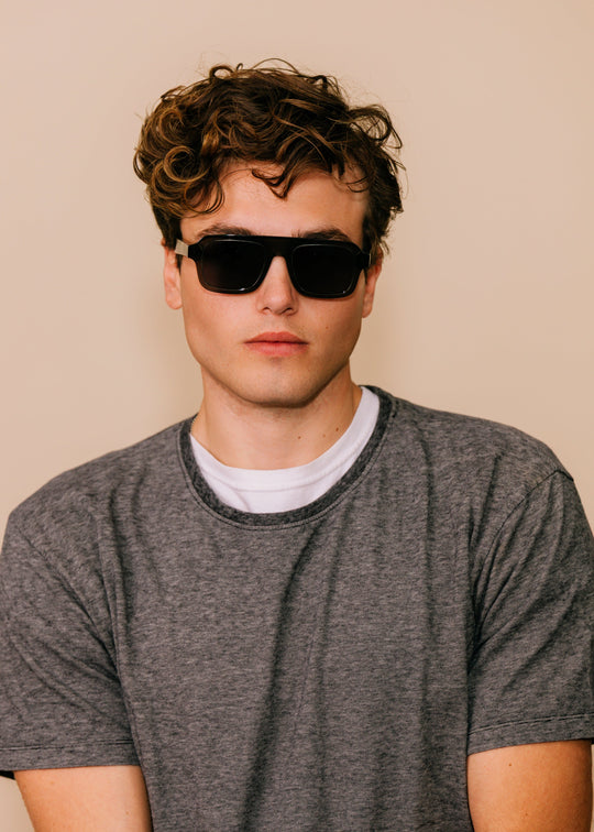 Man wearing sunglasses and a gray t-shirt against a beige background 