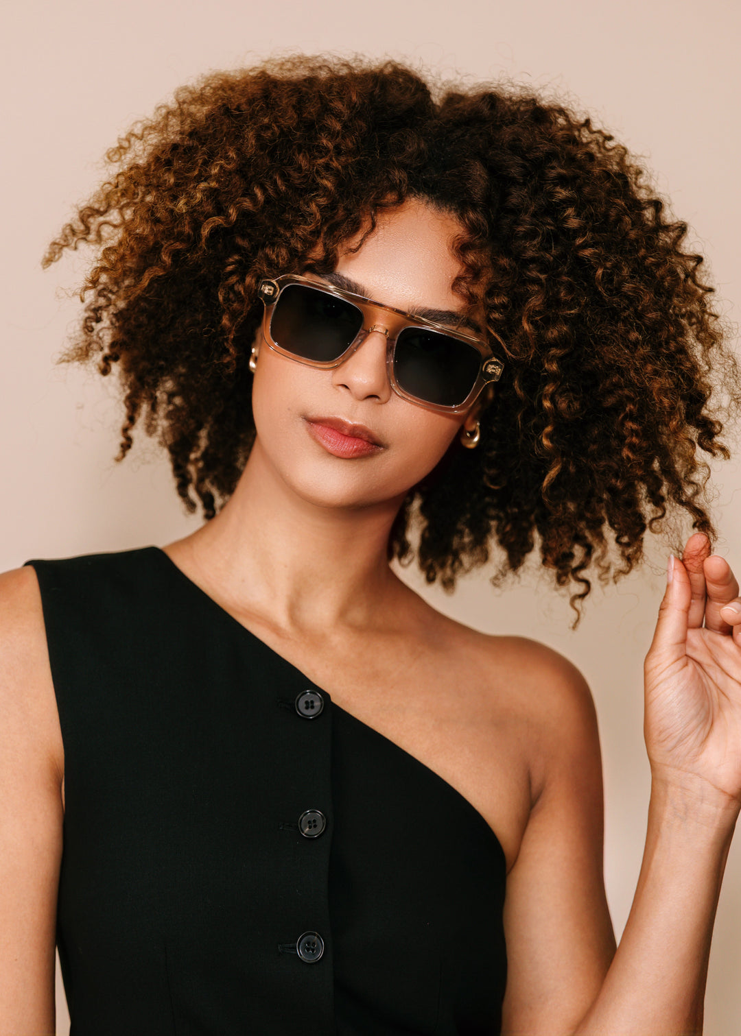 Woman wearing sunglasses and a black one-shoulder dress against a beige background