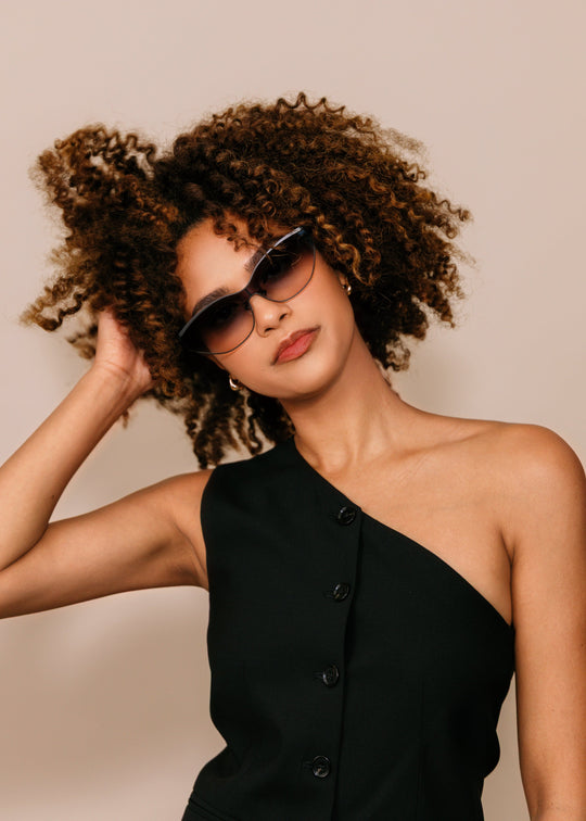 Model wearing Zenith sunglasses in Midnight Eclipse with a black one-shoulder dress against a neutral beige background. 