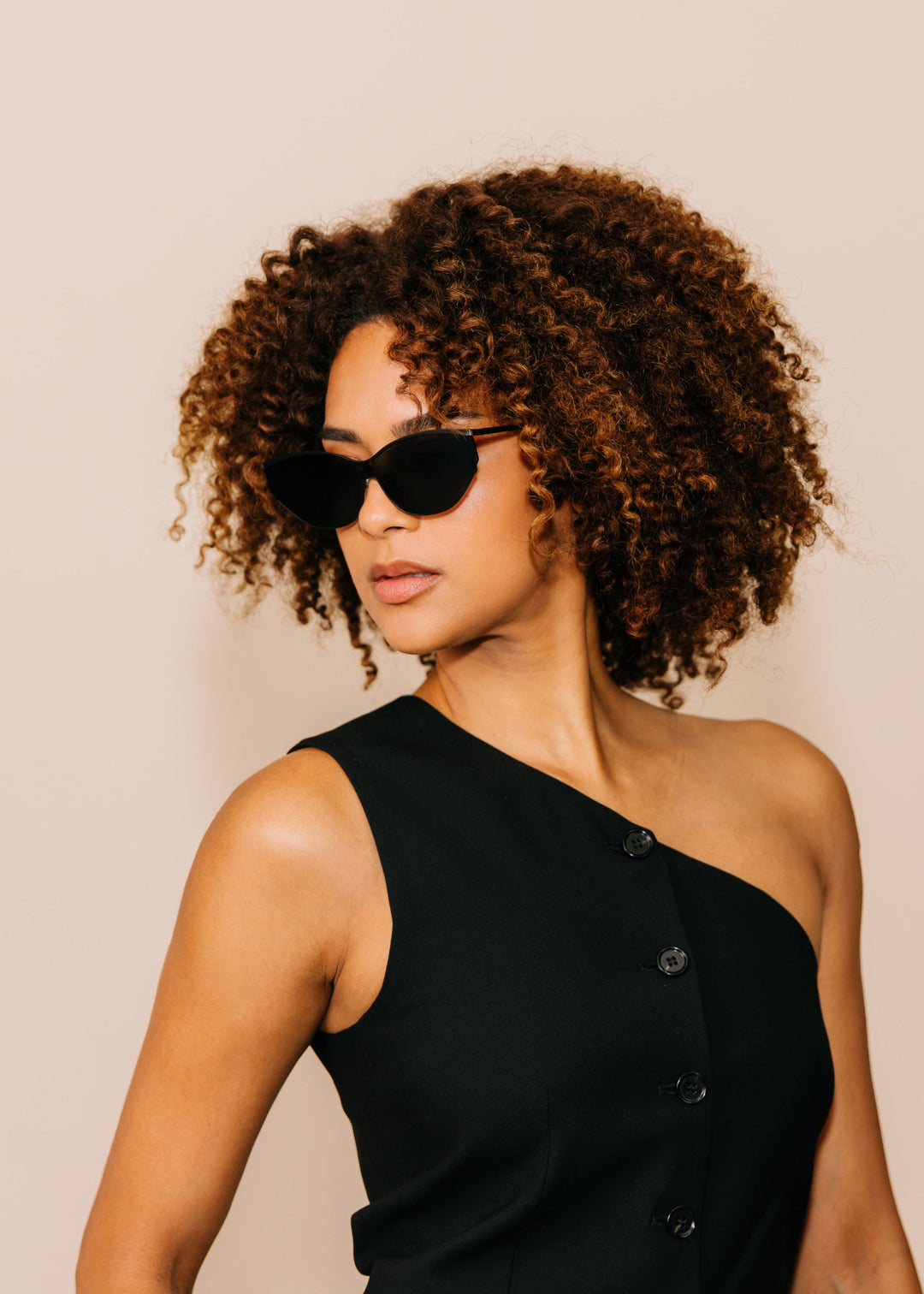 Model wearing Zenith sunglasses in Onyx Black with a black one-shoulder dress against a neutral beige background. 