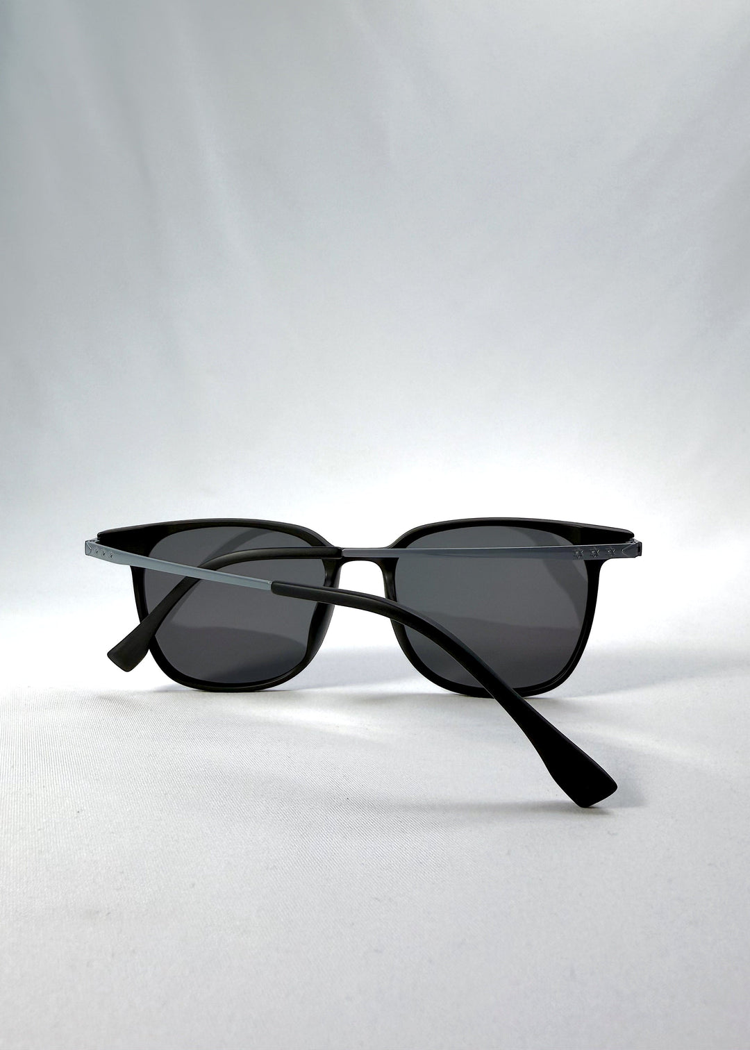 Folded view of Achernar sunglasses in Classic Black, featuring an ultra-light frame with titanium temples, softly geometric lens shape, and polarized lenses, showing the folded temples and frame profile. 