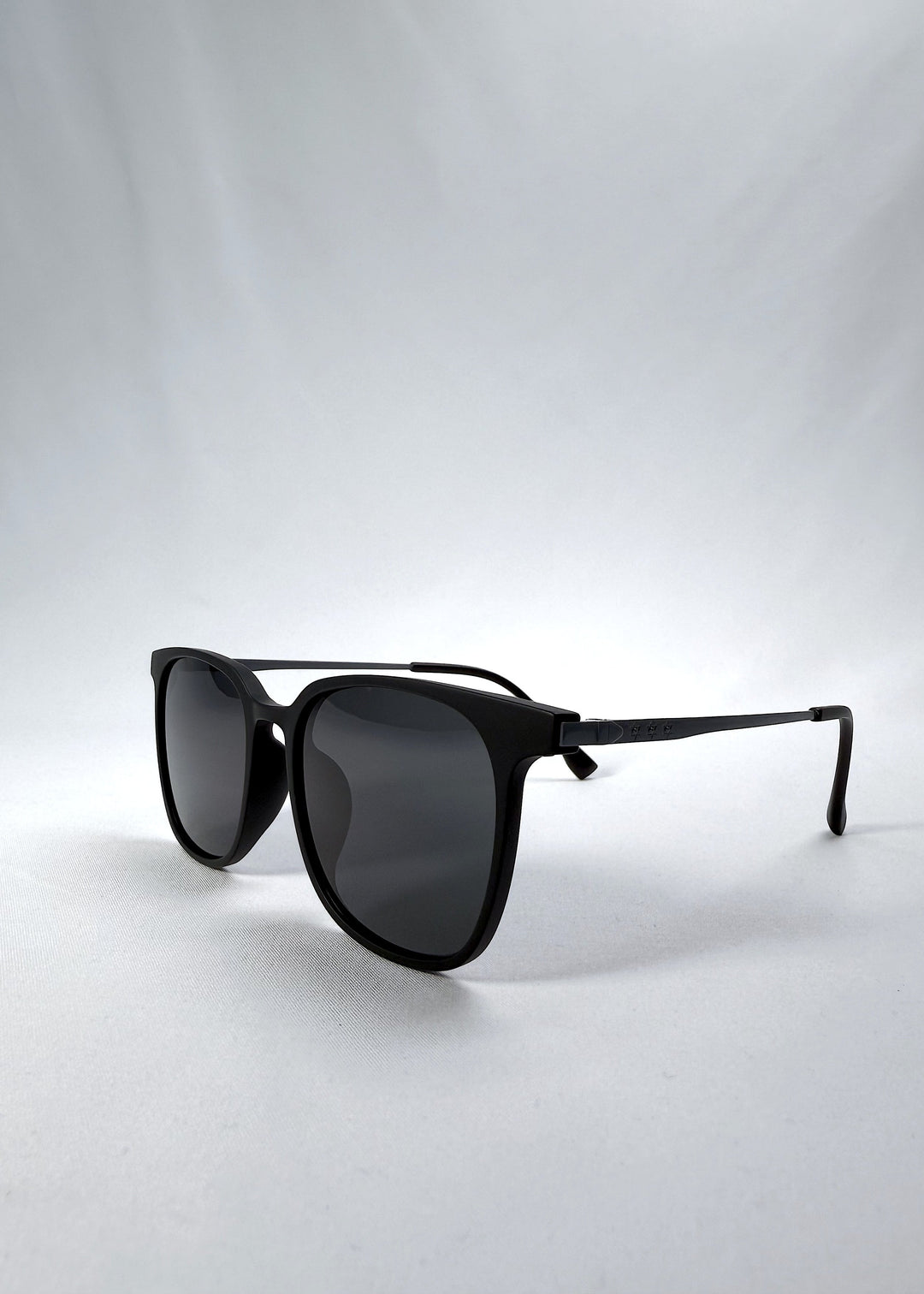 Three-quarter front view of Achernar sunglasses in Classic Black, featuring an ultra-light frame with titanium temples, softly geometric lens shape, and polarized lenses, showing the front shape and temple profile. 
