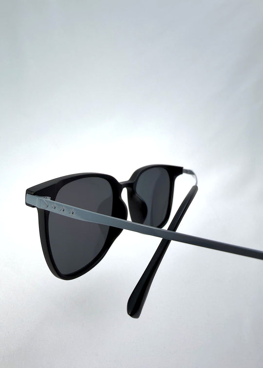 Close-up temple detail view of Achernar sunglasses in Classic Black, featuring an ultra-light frame with titanium temples, softly geometric lens shape, and polarized lenses, showing the temple arm and hinge area. 