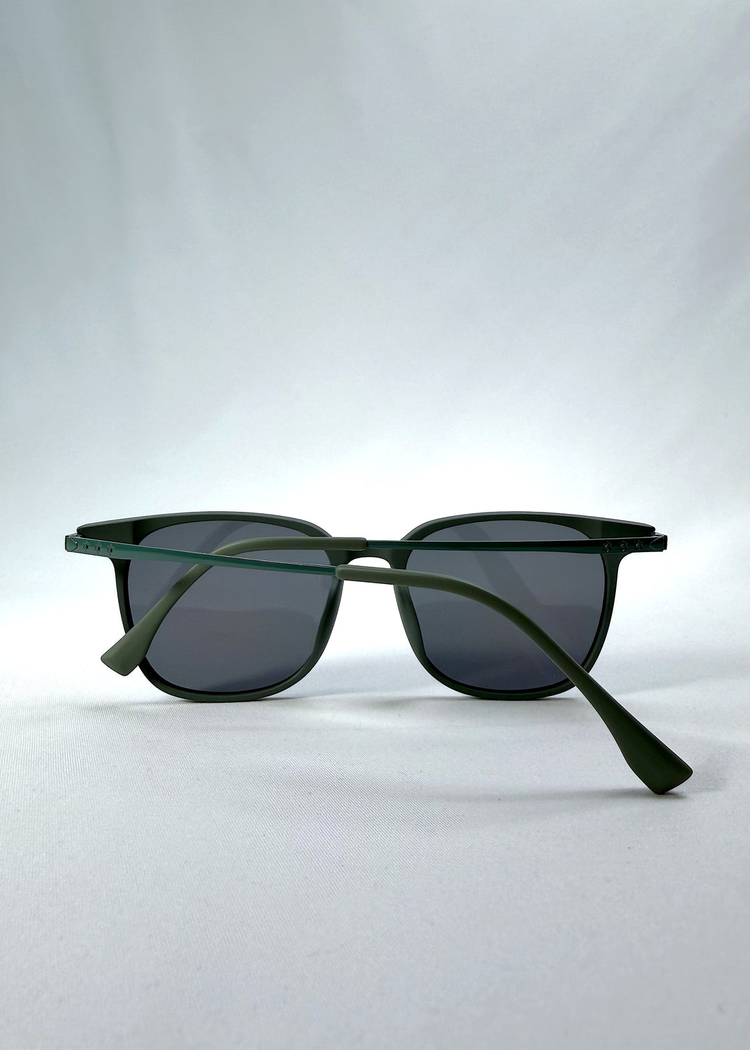 Folded view of Achernar sunglasses in Deep Matte Green, featuring ultra-light titanium frame, softly geometric lens shape, and polarized lenses, showing the folded temples and frame profile.