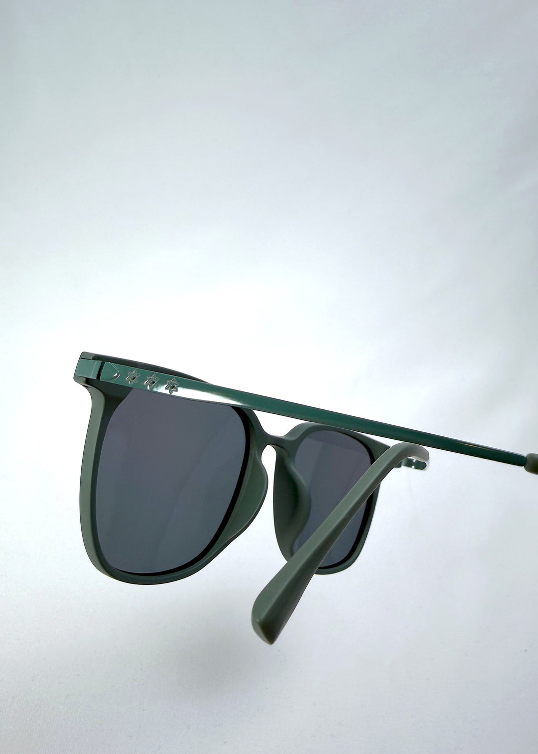 Close-up temple detail view of Achernar sunglasses in Deep Matte Green, featuring an ultra-light frame with titanium temples, softly geometric lens shape, and polarized lenses, showing the temple arm and hinge area. 