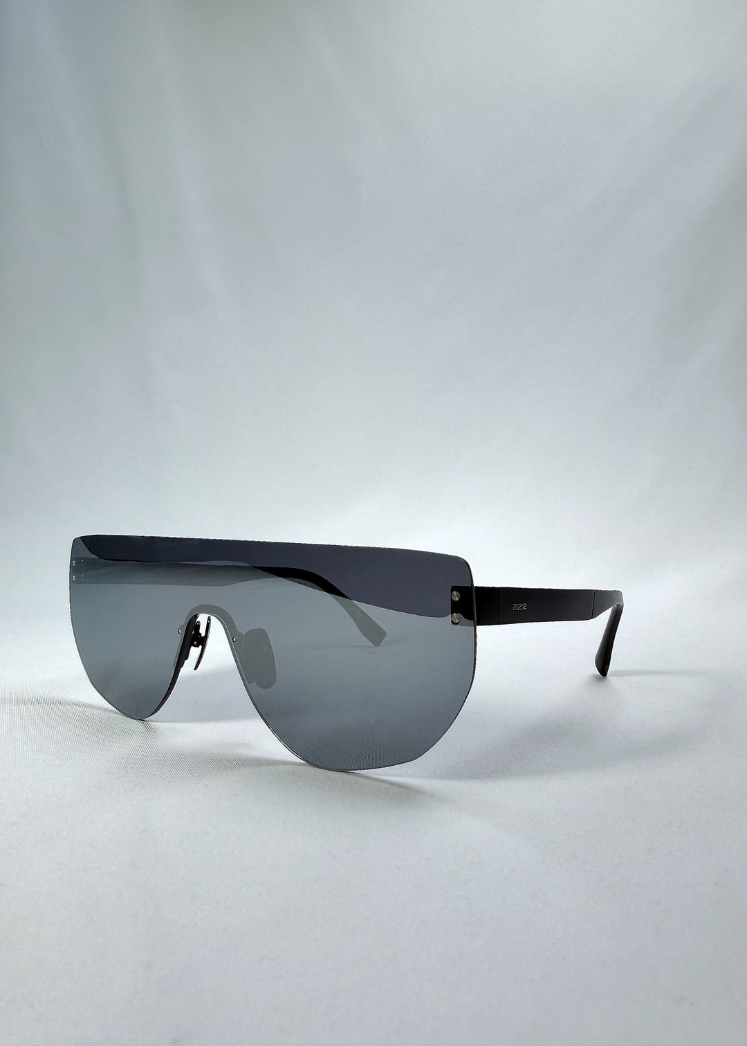 Three-quarter front view of Aegis Field sunglasses in Mercury Shadow, featuring one-piece titanium shield frame and silver mirrored lens, showing the front shape and temple profile. 
