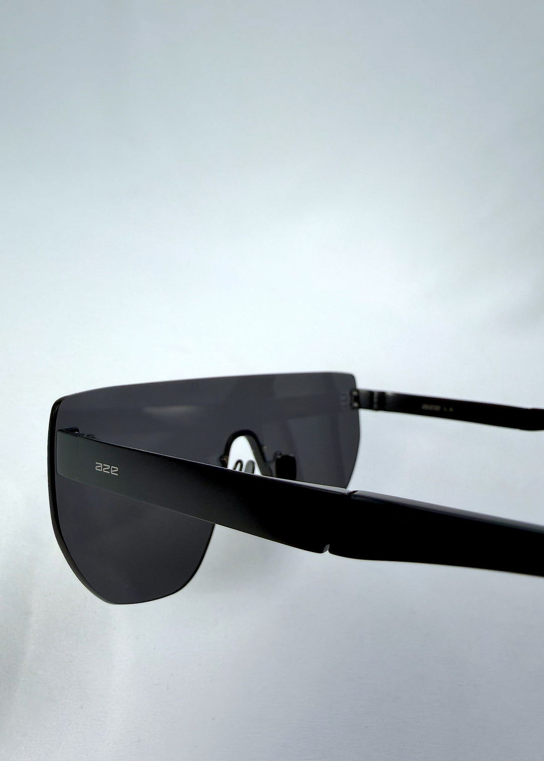 Close-up side detail view of Aegis Field sunglasses in Obsidian Black, featuring one-piece titanium shield frame and smoky black lens, showing the lens edge, hinge area, and temple detail. 