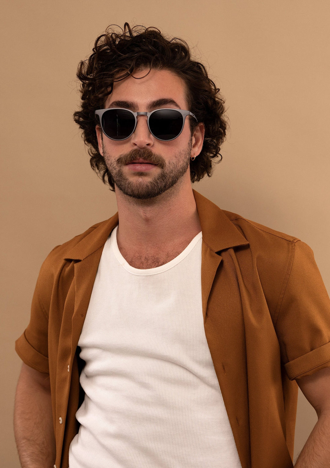Male model wearing Altair sunglasses in Matte Gray with a camel jacket over a white top, facing forward. 