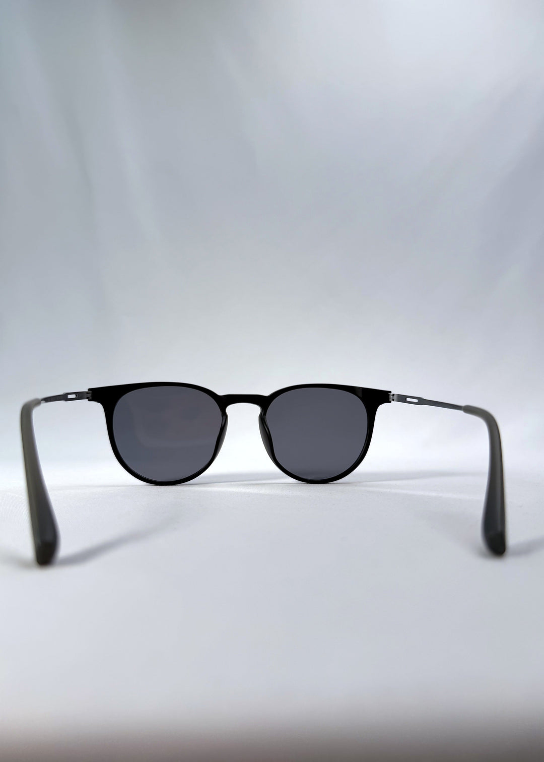 Back view of Altair sunglasses in Matte Black, featuring a minimal frame with titanium temples, rounded square lens shape, and polarized lenses, showing the inside frame and open temples. 