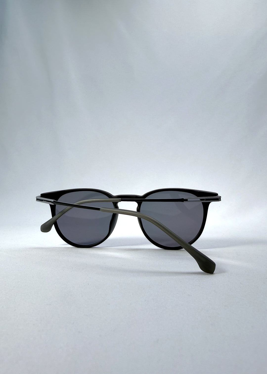 Folded view of Altair sunglasses in Matte Black, featuring a minimal frame with titanium temples, rounded square lens shape, and polarized lenses, showing the folded temples and frame profile. 