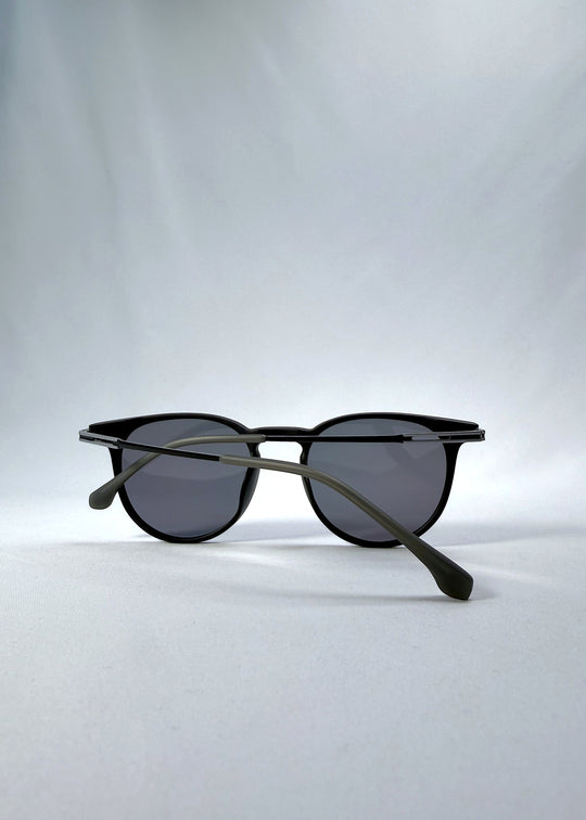 Folded view of Altair sunglasses in Matte Black, featuring a minimal frame with titanium temples, rounded square lens shape, and polarized lenses, showing the folded temples and frame profile. 