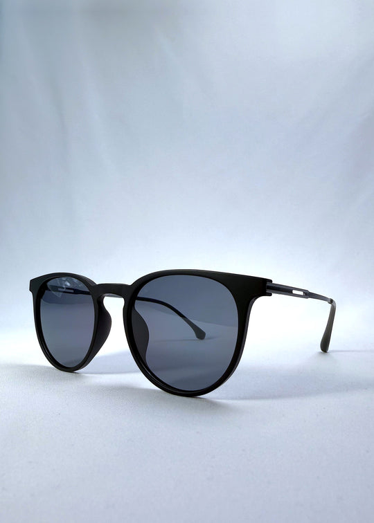 Three-quarter front view of Altair sunglasses in Matte Black, featuring a minimal frame with titanium temples, rounded square lens shape, and polarized lenses, showing the front shape and temple profile. 