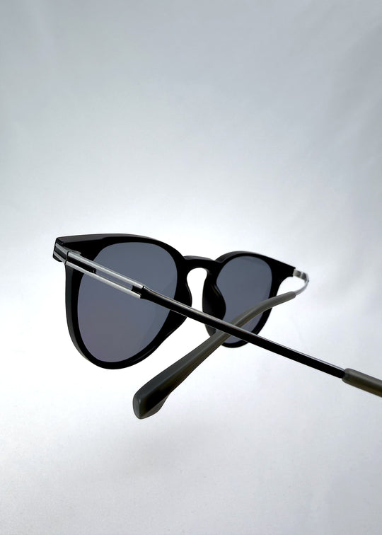 Close-up temple detail view of Altair sunglasses in Matte Black, featuring a minimal frame with titanium temples, rounded square lens shape, and polarized lenses, showing the temple arm and hinge area. 