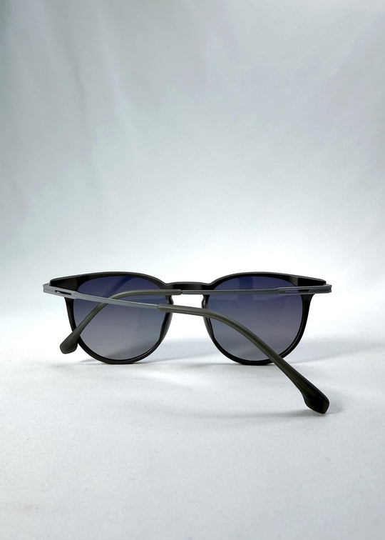 Folded view of Altair sunglasses in Matte Gray, featuring minimal titanium frame, rounded square lens shape, and polarized lenses, showing the folded temples and frame profile.