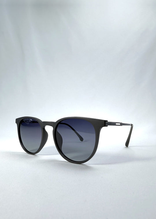 Three-quarter front view of Altair sunglasses in Matte Gray, featuring a minimal frame with titanium temples, rounded square lens shape, and polarized lenses, showing the front shape and temple profile. 