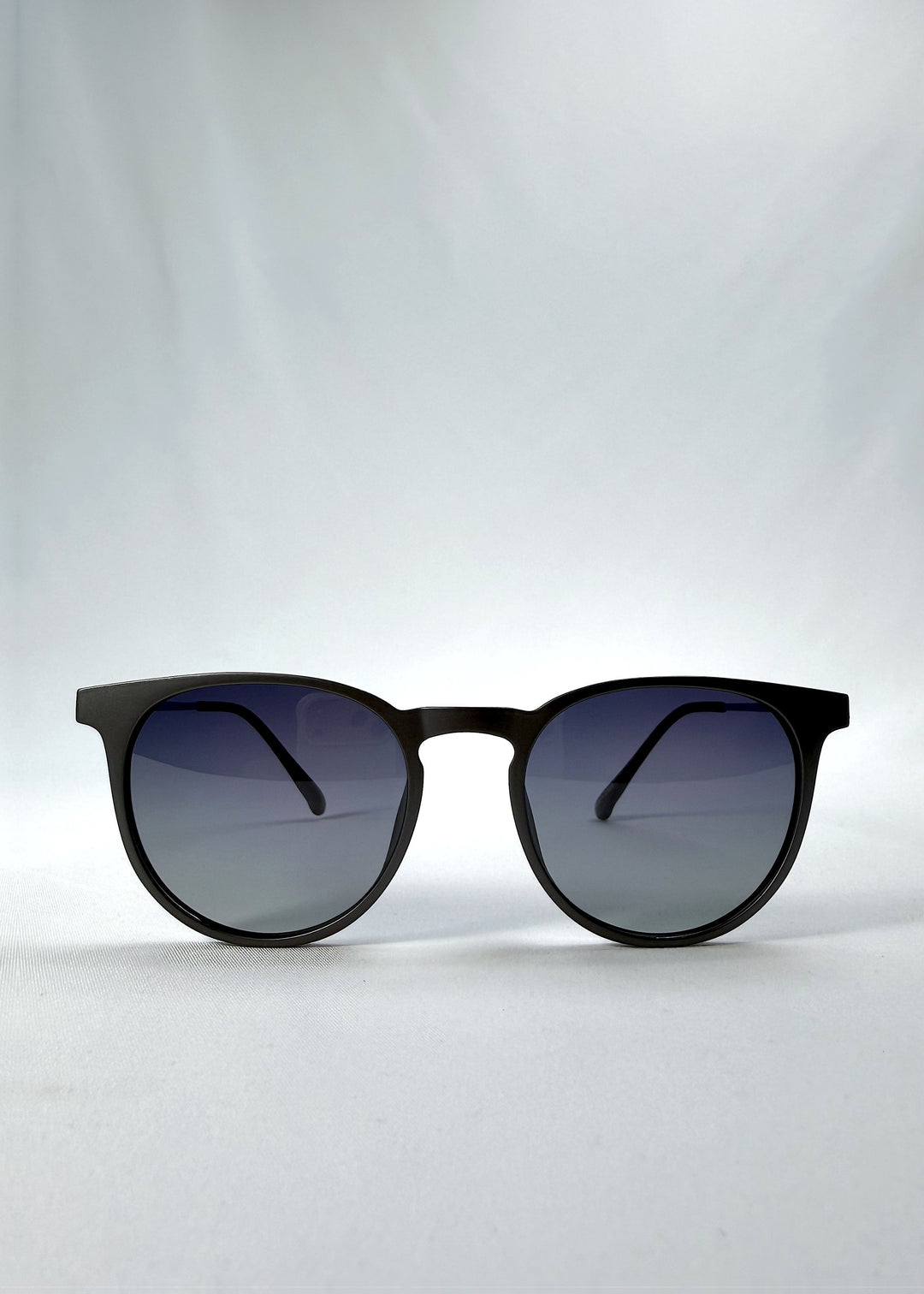 Front view of Altair sunglasses in Matte Gray, featuring a minimal frame with titanium temples, rounded square lens shape, and polarized lenses, showing the full front silhouette. 