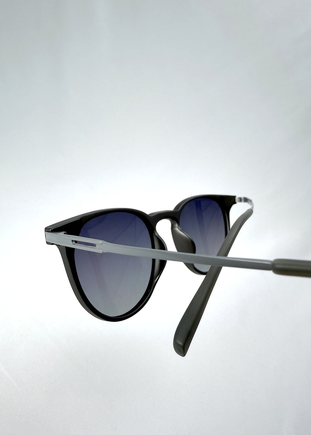 Close-up temple detail view of Altair sunglasses in Matte Gray, featuring a minimal frame with titanium temples, rounded square lens shape, and polarized lenses, showing the temple arm and hinge area. 
