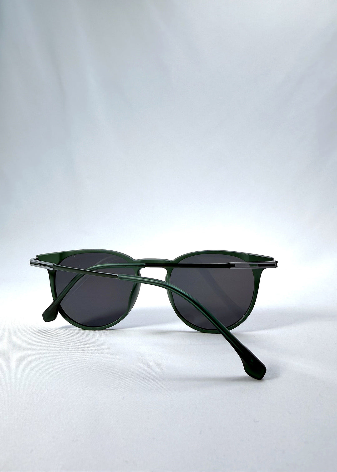 Folded view of Altair sunglasses in Matte Green, featuring a minimal frame with titanium temples, rounded square lens shape, and polarized lenses, showing the folded temples and frame profile. 