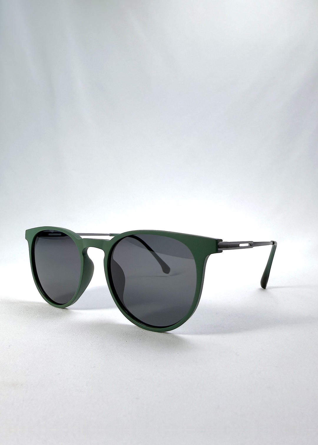 Three-quarter front view of Altair sunglasses in Matte Green, featuring a minimal frame with titanium temples, rounded square lens shape, and polarized lenses, showing the front shape and temple profile. 