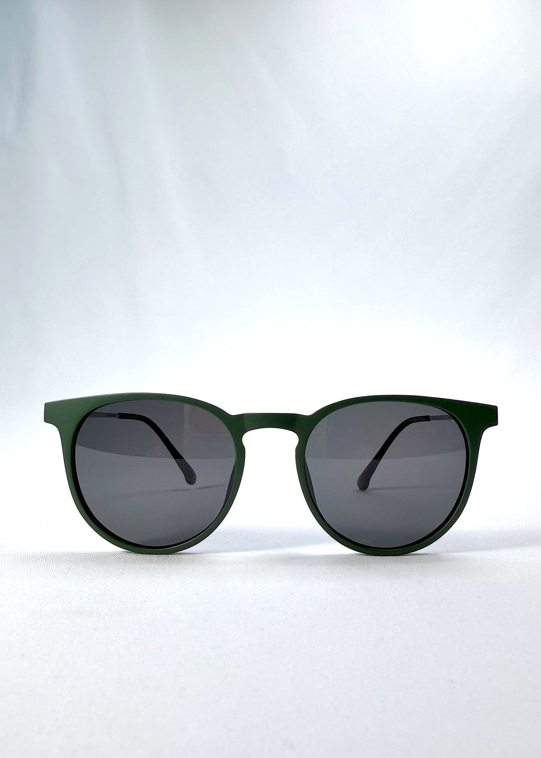 Front view of Altair sunglasses in Matte Green, featuring a minimal frame with titanium temples, rounded square lens shape, and polarized lenses, showing the full front silhouette. 