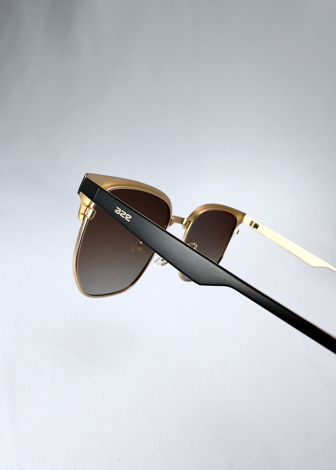 Closeup of the temple on Altessa sunglasses in Antique Brass showing the AZE logo and black matte finish. 