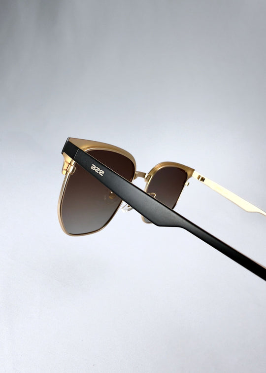 Closeup of the temple on Altessa sunglasses in Antique Brass showing the AZE logo and black matte finish. 