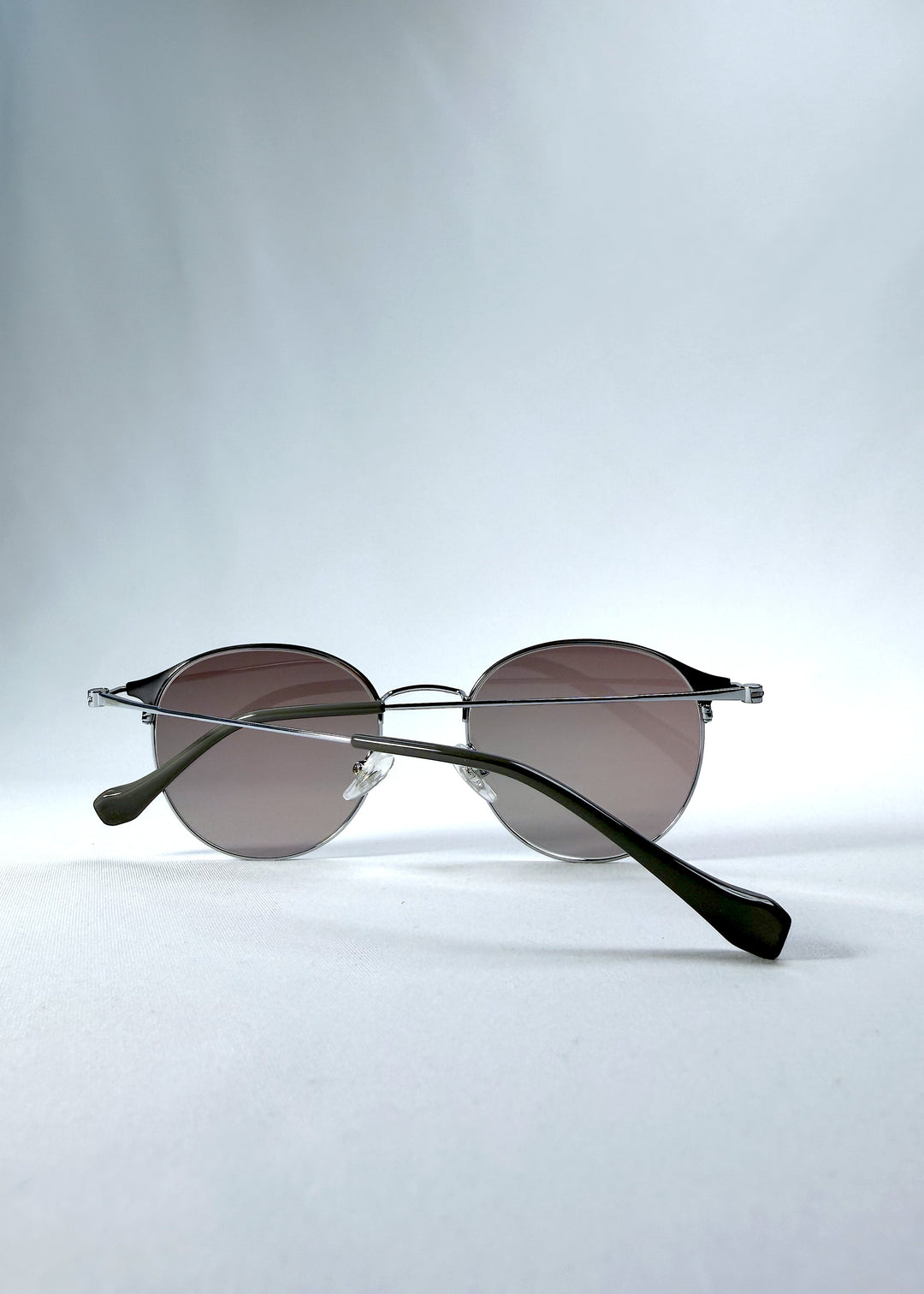 Folded view of AZE Aster Line sunglasses in Mocha Dusk, featuring a silver-tone rounded frame and taupe gradient lenses, showing the folded temples and frame profile.