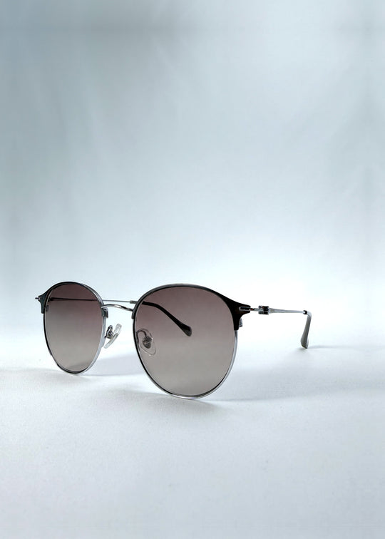 Three-quarter front view of AZE Aster Line sunglasses in Mocha Dusk, featuring a silver-tone rounded frame and taupe gradient lenses, showing the frame shape and temple profile.