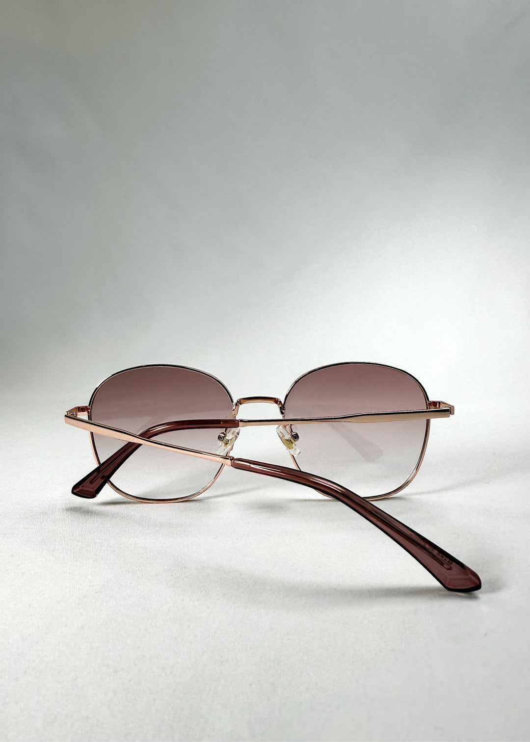 Folded view of Astris – Rosé Dawn sunglasses with rosy temples crossed over the gradient lenses. 
