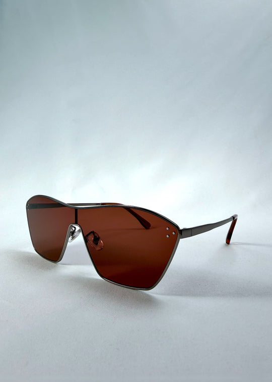 Three-quarter front view of Atlas Shield sunglasses in Ruby Smoke, featuring one-piece shield lens, slim metal frame, and wine-red tint, showing the front shape and temple profile.
