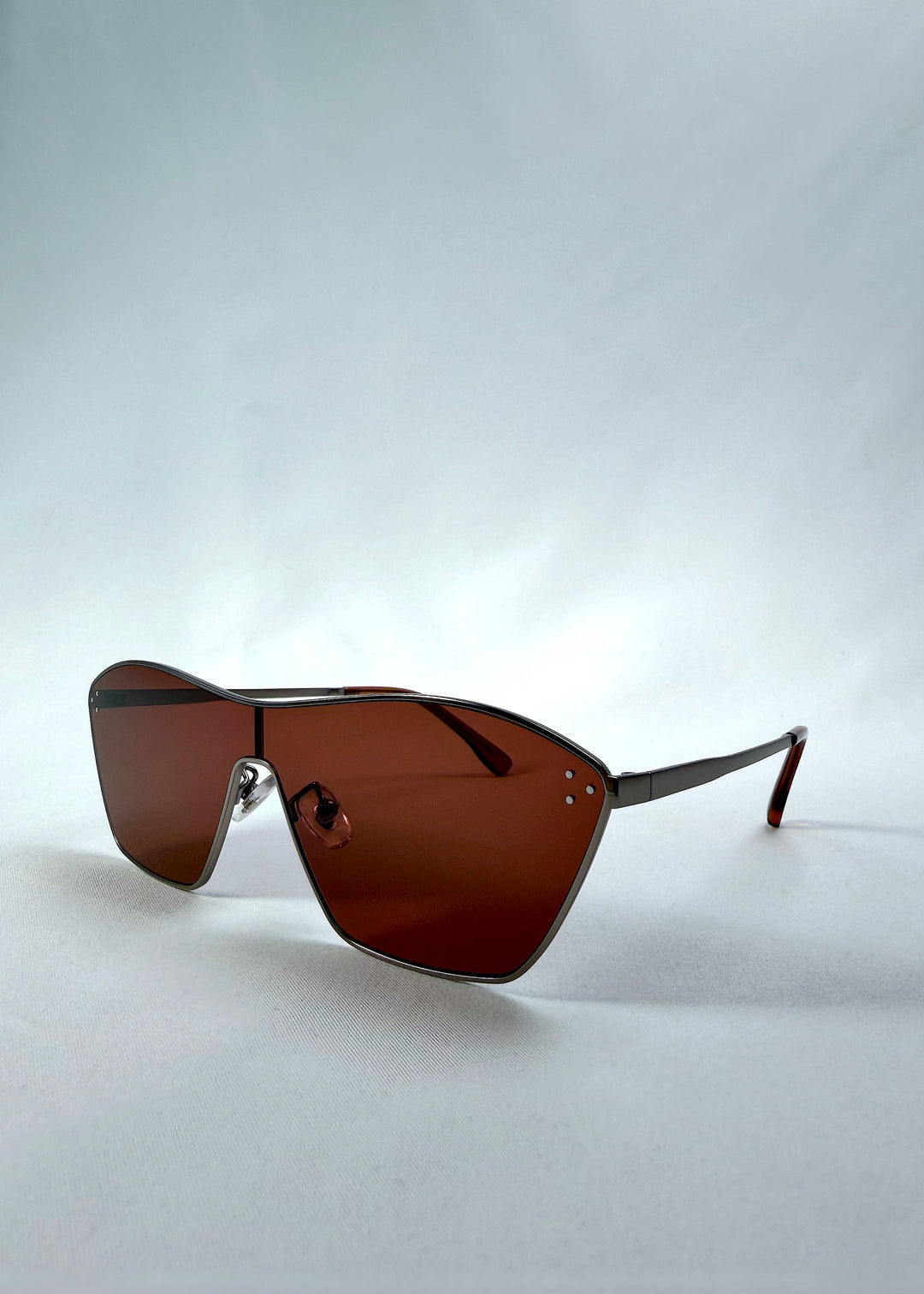 Three-quarter front view of Atlas Shield sunglasses in Ruby Smoke, featuring one-piece shield lens, slim metal frame, and wine-red tint, showing the front shape and temple profile. 