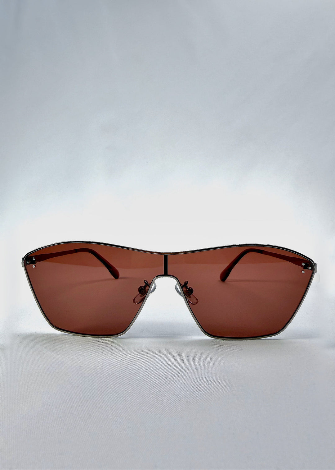 Front view of Atlas Shield sunglasses in Ruby Smoke, featuring one-piece shield lens, slim metal frame, and wine-red tint, showing the full front silhouette. 