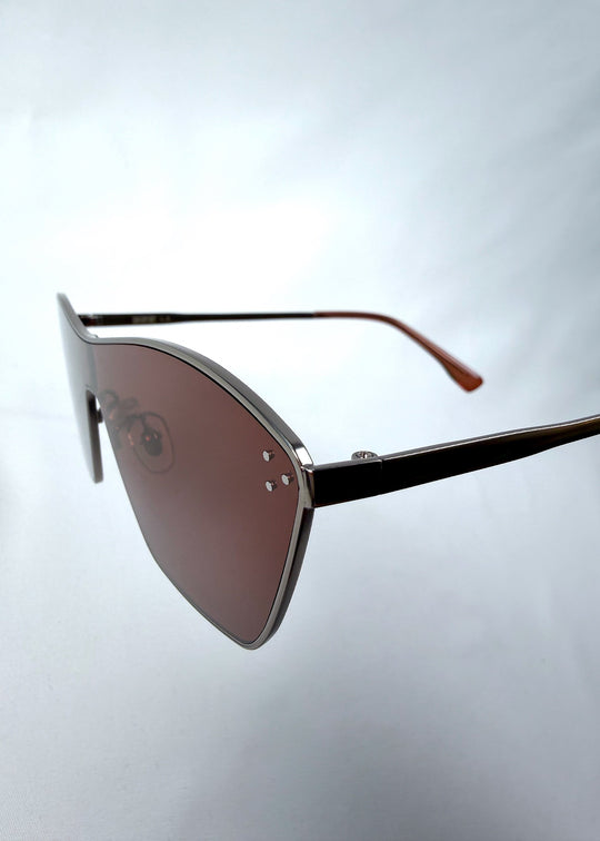 Close-up side detail view of Atlas Shield sunglasses in Ruby Smoke, featuring one-piece shield lens, slim metal frame, and wine-red tint, showing the lens edge, hinge area, and temple detail. 