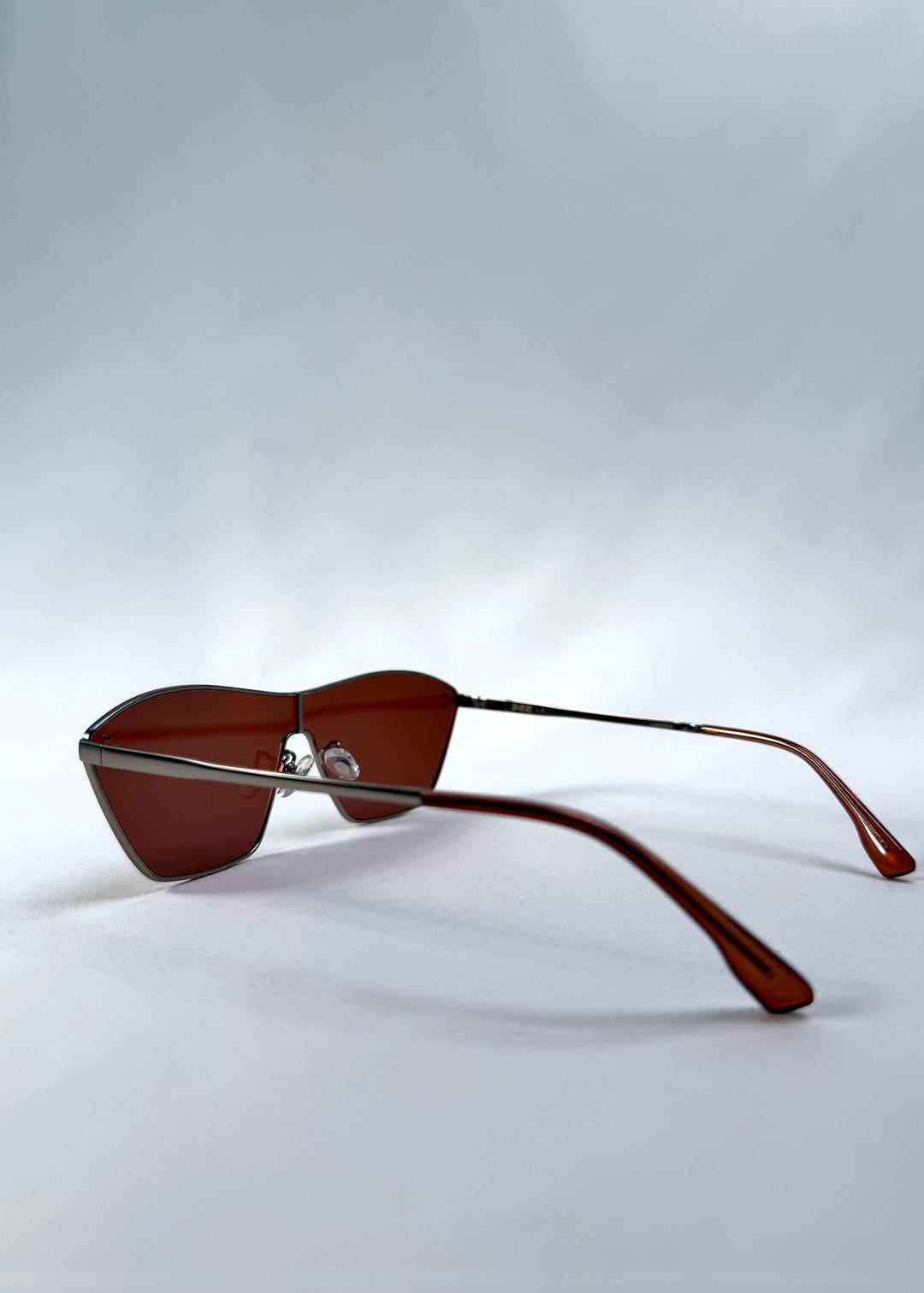 Side view of Atlas Shield sunglasses in Ruby Smoke, featuring one-piece shield lens, slim metal frame, and wine-red tint, showing the lens shape and temple profile. 