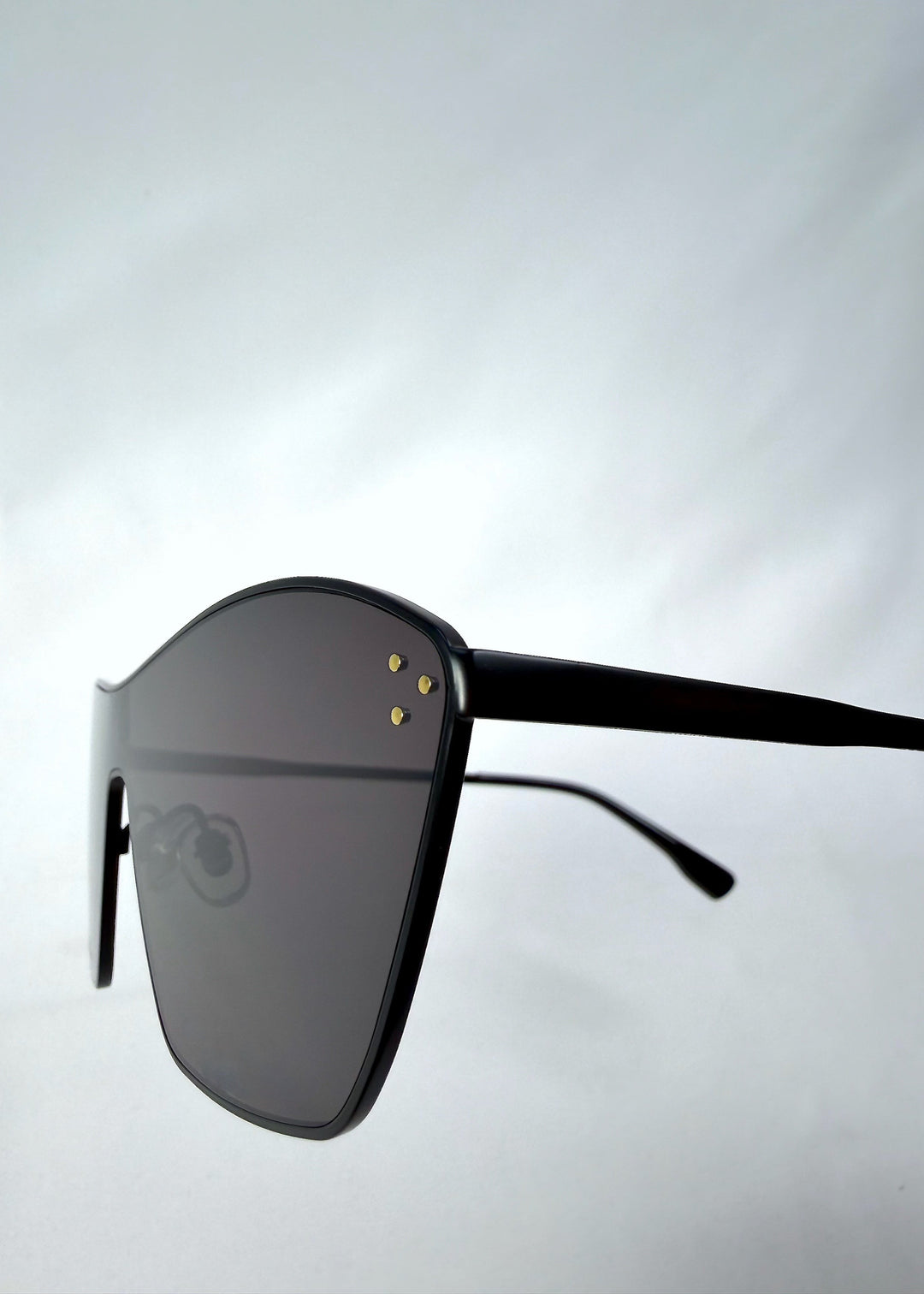 Close-up side detail view of Atlas Shield sunglasses in Slate Smoke, featuring one-piece shield lens, slim metal frame, and full grey tint, showing the lens edge, hinge area, and temple detail. 