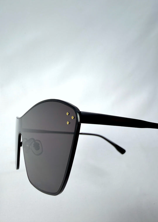 Close-up side detail view of Atlas Shield sunglasses in Slate Smoke, featuring one-piece shield lens, slim metal frame, and full grey tint, showing the lens edge, hinge area, and temple detail. 