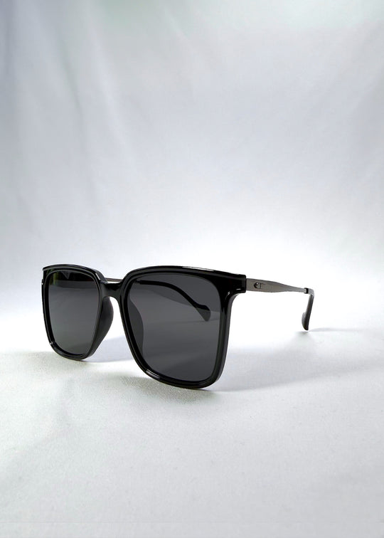 Three-quarter front view of Auralis sunglasses in Duskgold, featuring black and gold frame with dark lenses, showing the front shape and temple profile.