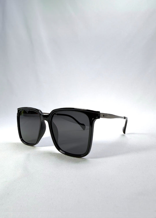 Three-quarter front view of Auralis sunglasses in Duskgold, featuring black and gold frame with dark lenses, showing the front shape and temple profile. 
