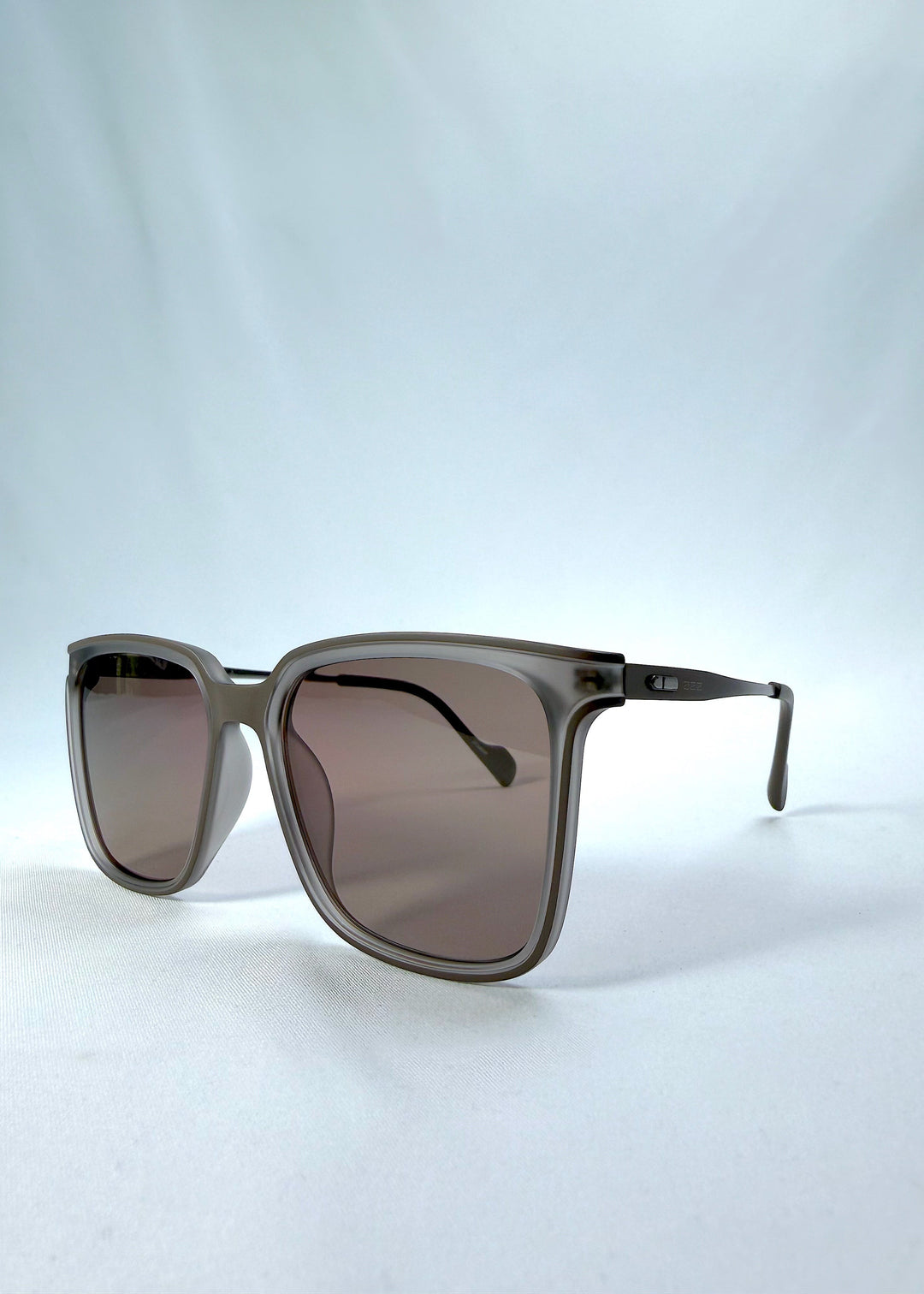 Three-quarter front view of Auralis sunglasses in Sand Amber, featuring sand amber frame and brown lenses, showing the front shape and temple profile. 