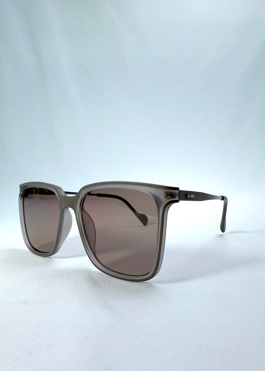 Three-quarter front view of Auralis sunglasses in Sand Amber, featuring sand amber frame and brown lenses, showing the front shape and temple profile. 