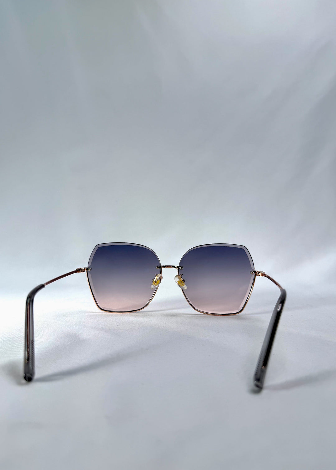 Back view of Aureon sunglasses in Rosé Quartz, featuring rimless metal frame, pale metal temples, and pink-grey gradient lenses, showing the inside frame and open temples. 