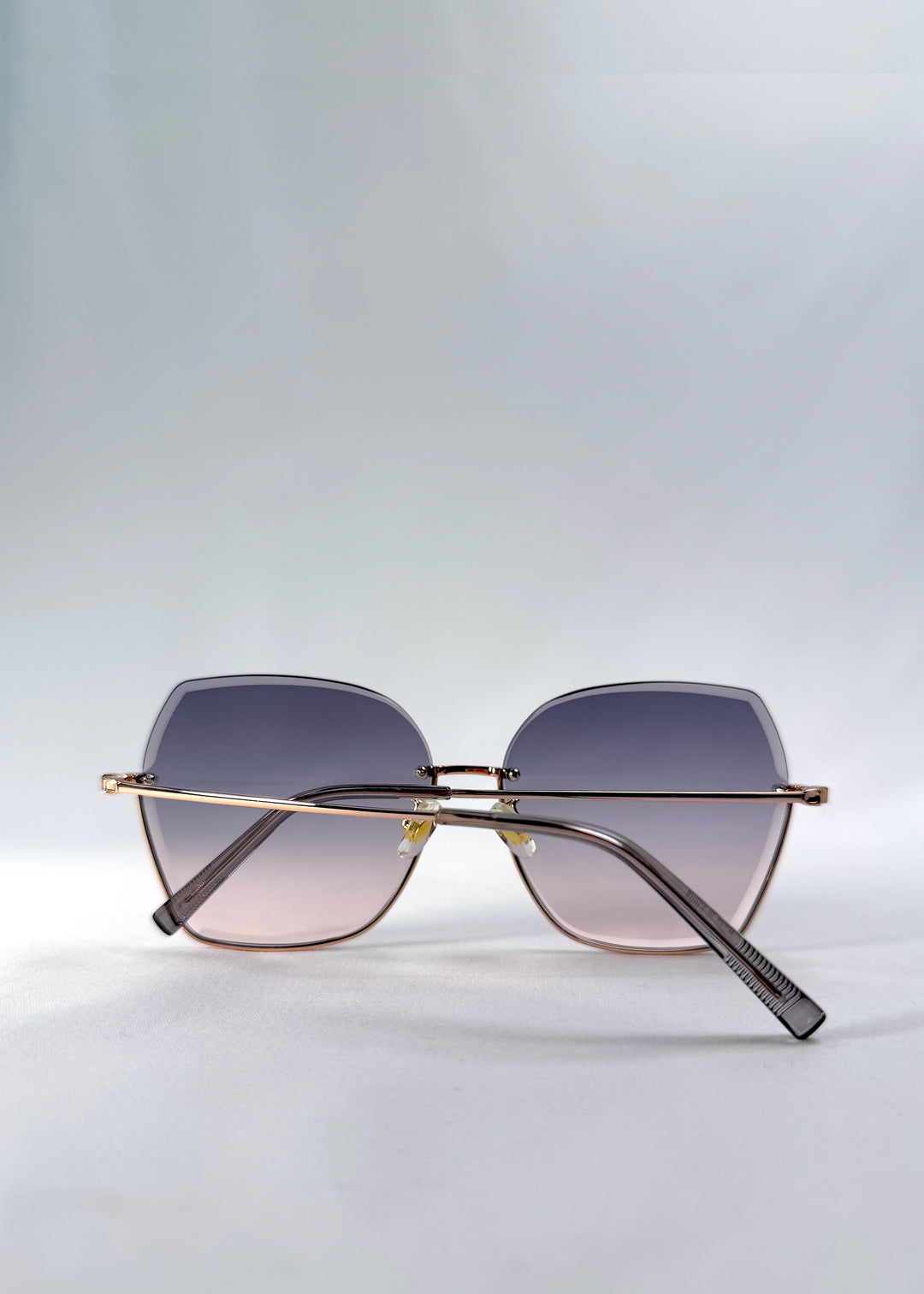 Folded view of Aureon sunglasses in Rosé Quartz, featuring rimless metal frame, pale metal temples, and pink-grey gradient lenses, showing the folded temples and frame profile.