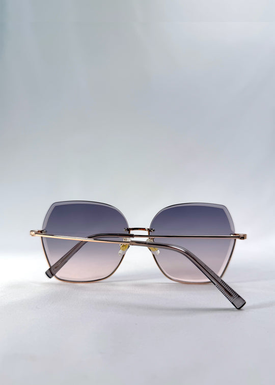 Folded view of Aureon sunglasses in Rosé Quartz, featuring rimless metal frame, pale metal temples, and pink-grey gradient lenses, showing the folded temples and frame profile.